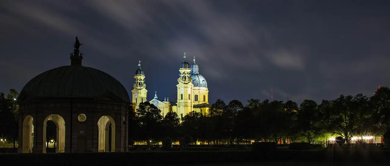 El templo redondo del Hofgarten de noche, con torres de iglesia iluminadas detrás