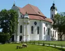 La Wieskirche blanca, con su campanario, sobre un prado verde con dos ponis pastando