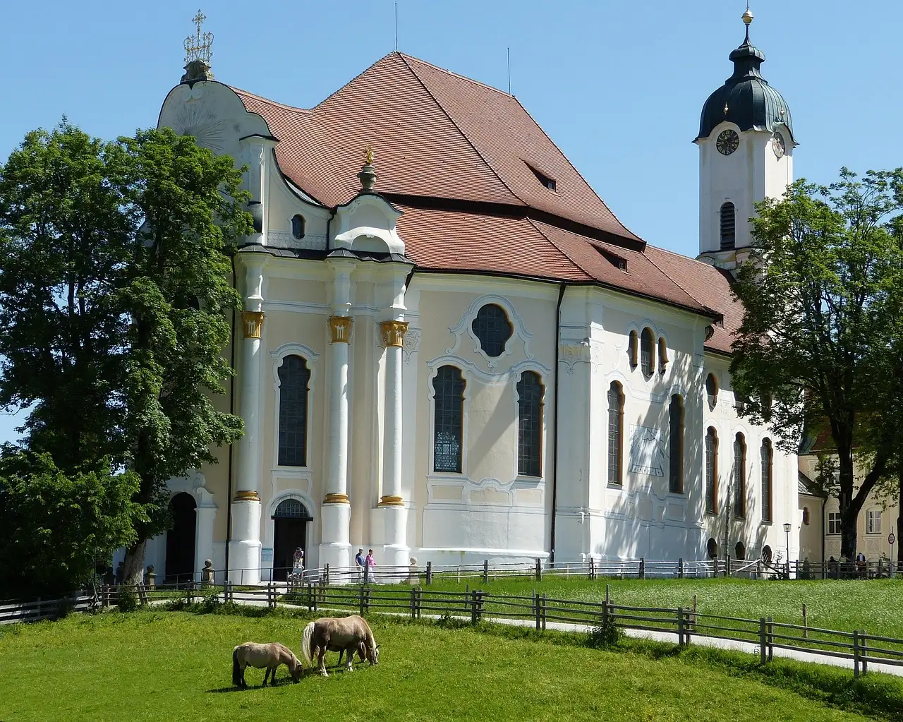 La Wieskirche blanca, con su campanario, sobre un prado verde con dos ponis pastando