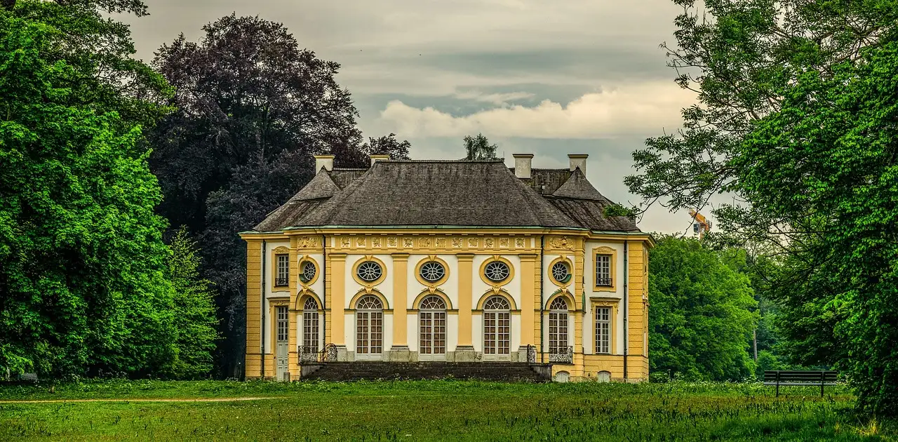 Un pabellón amarillo con tejado gris entre árboles verdes altos en el parque de Nymphenburg