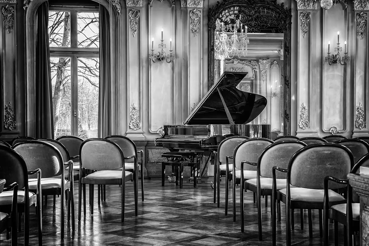 Una foto en blanco y negro de un piano de cola en una sala decorada con filas de sillas