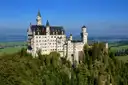 El castillo de Neuschwanstein en su roca sobre un bosque verde, con la llanura y un lago detrás