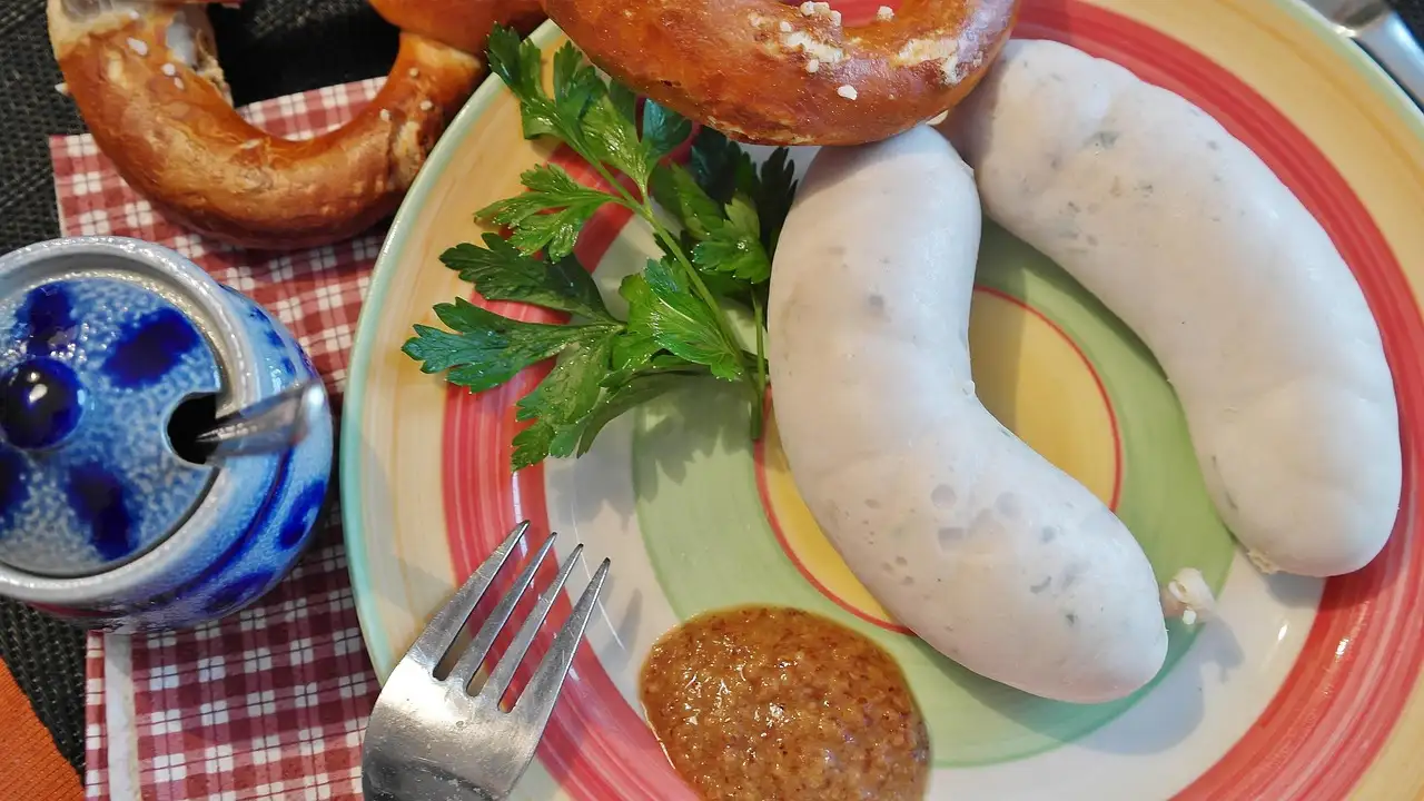 Dos salchichas blancas bávaras de ternera en un plato con mostaza dulce y un pretzel