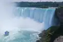 Las cataratas Horseshoe de día, con el agua verde, la bruma que sube y un barco turístico abajo