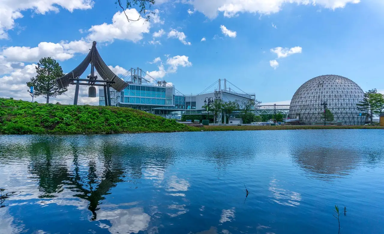 La cúpula de la Cinesphere y los pabellones de Ontario Place se reflejan en una laguna azul bajo un cielo luminoso con nubes.