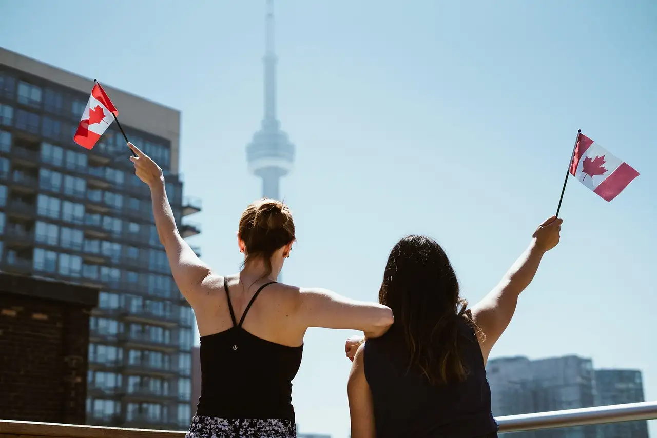 Dos personas de espaldas agitan banderitas de Canadá, con la Torre CN detrás
