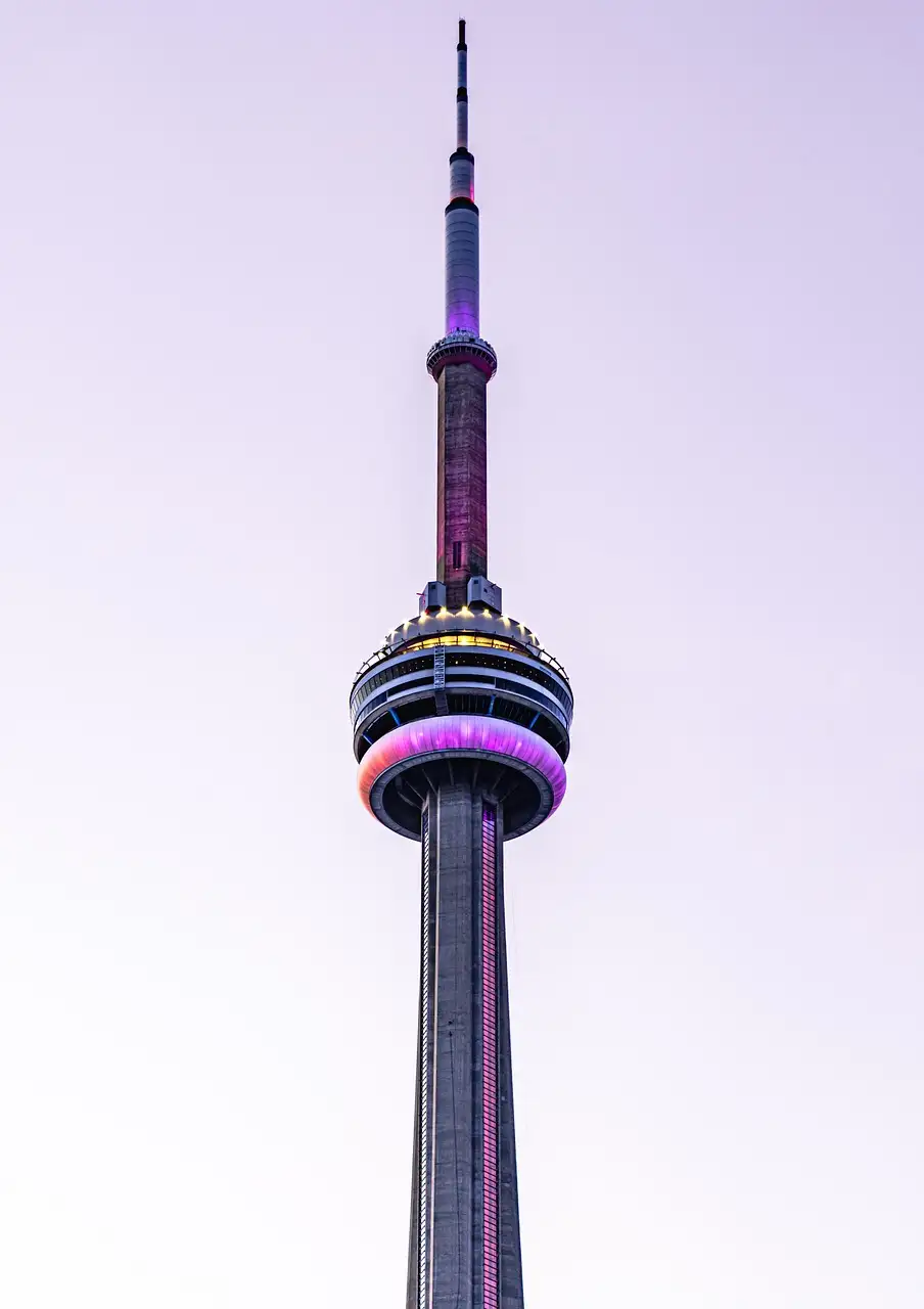 La parte alta de la Torre CN, con la cápsula iluminada en rosa y morado, sobre un cielo pálido