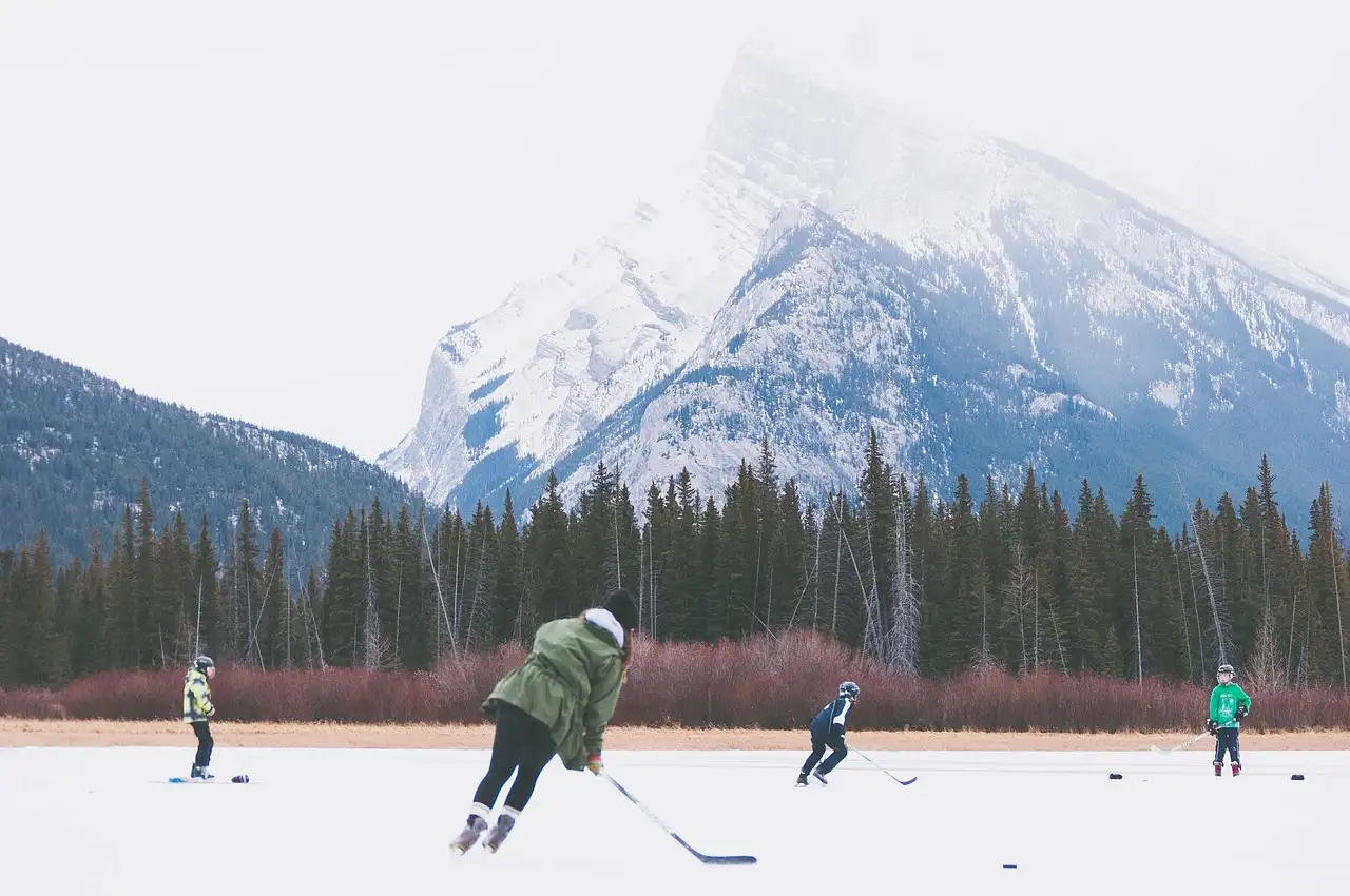 Gente jugando al hockey en un lago helado bajo una montaña nevada