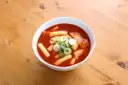 Un cuenco blanco de pasteles de arroz coreanos en salsa roja de chile sobre una mesa de madera clara