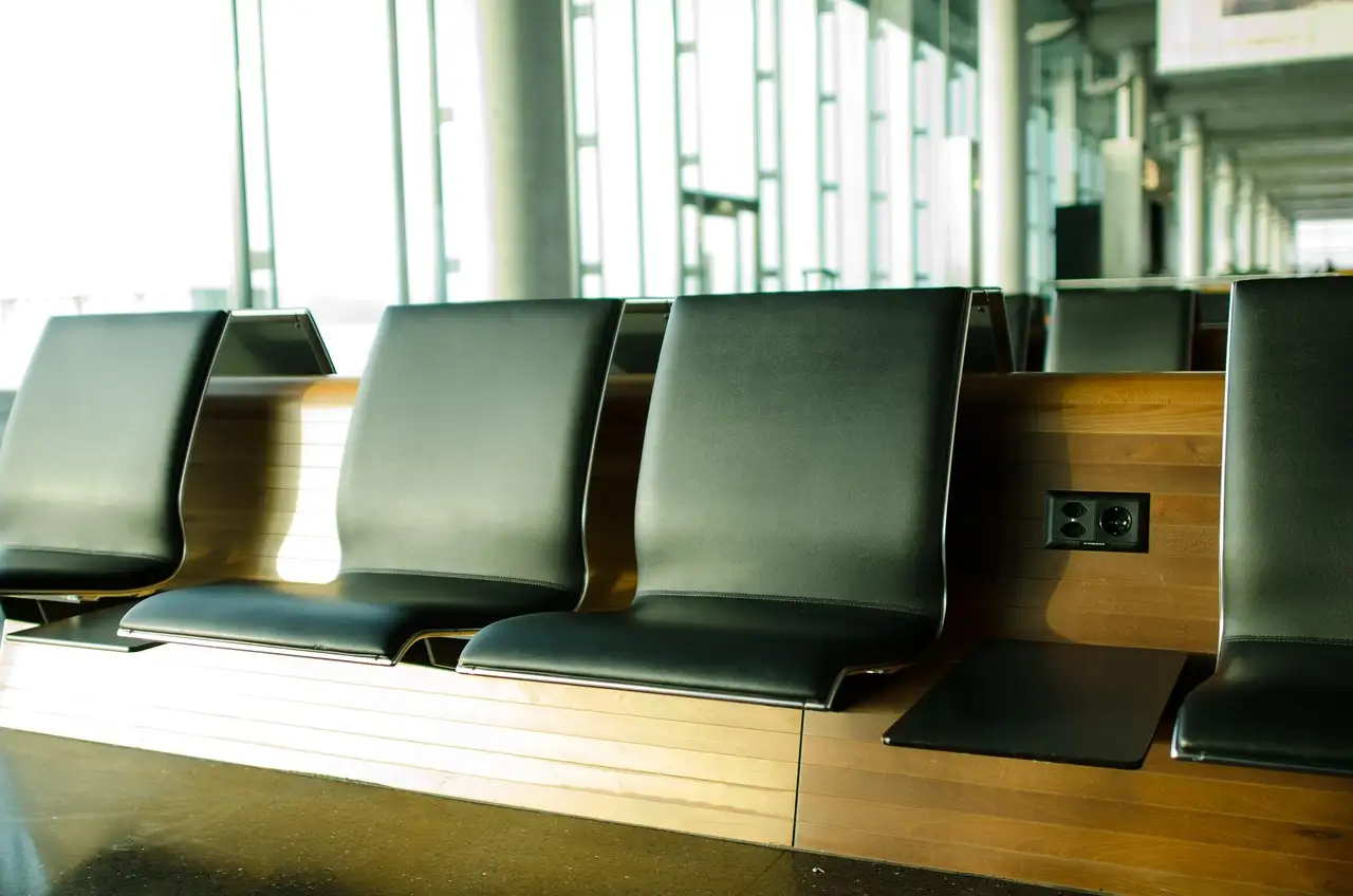 Filas de asientos de cuero oscuro junto a grandes ventanales en una sala de espera de aeropuerto