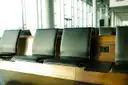 Filas de asientos de cuero oscuro junto a grandes ventanales en una sala de espera de aeropuerto