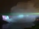 Las cataratas Horseshoe iluminadas de noche en morado y azul, con bruma encima
