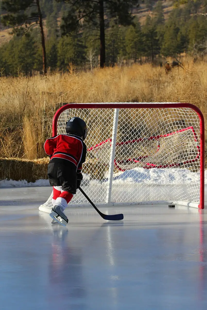 Un niño con camiseta roja de hockey patina hacia una portería en una pista al aire libre