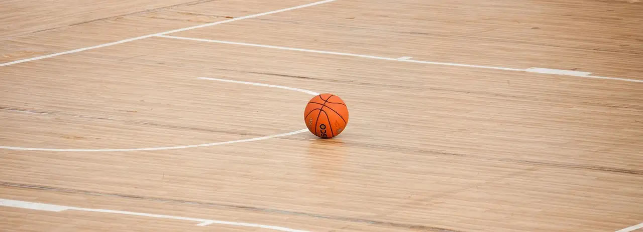 Un balón de baloncesto naranja en el suelo de madera de una pista cubierta vacía
