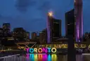 Las torres curvas del ayuntamiento de Toronto iluminadas en morado sobre el letrero de colores de Toronto y el estanque de Nathan Phillips Square al anochecer.