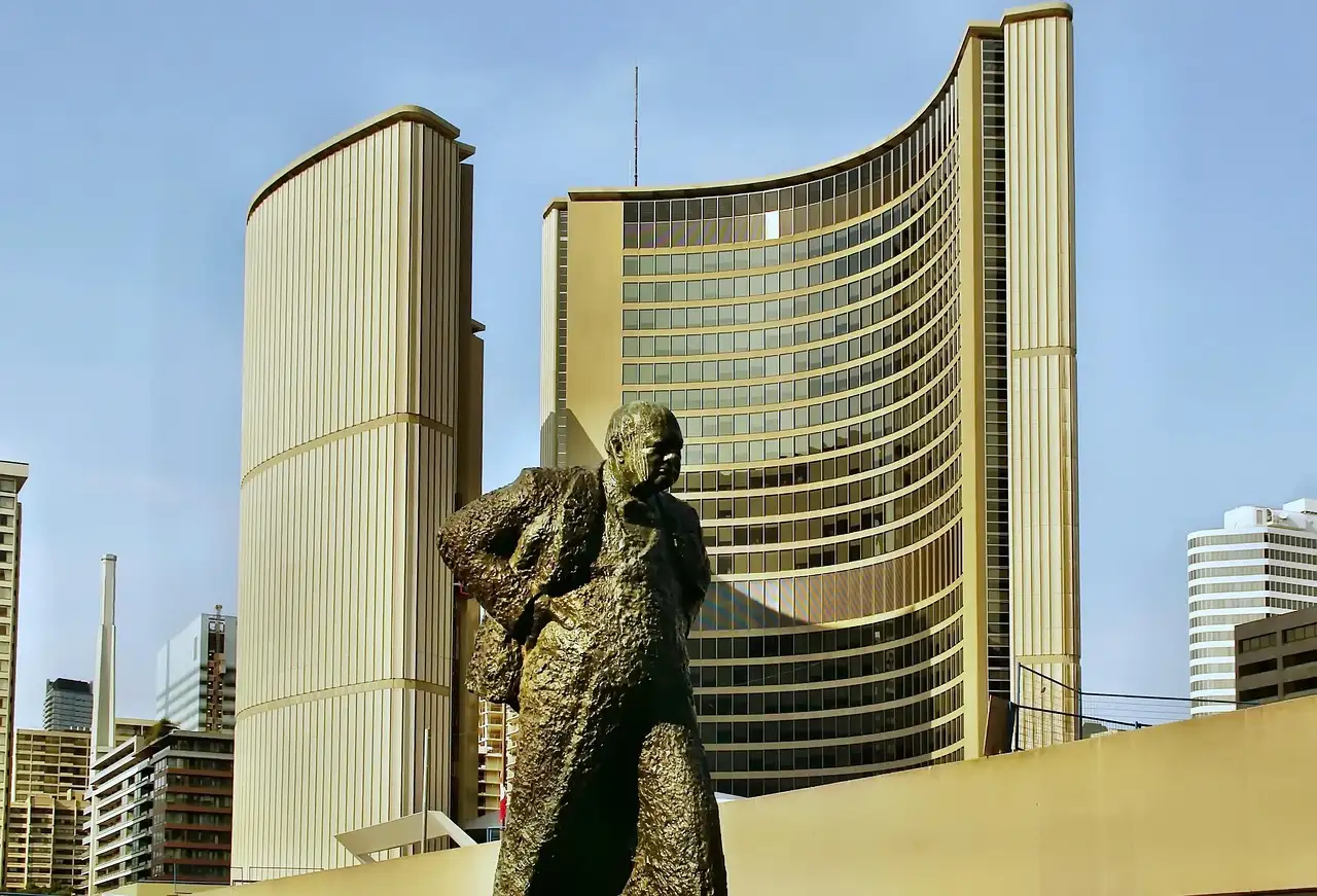 Las torres curvas del Ayuntamiento de Toronto bajo el sol, con una estatua de bronce delante, en Nathan Phillips Square.