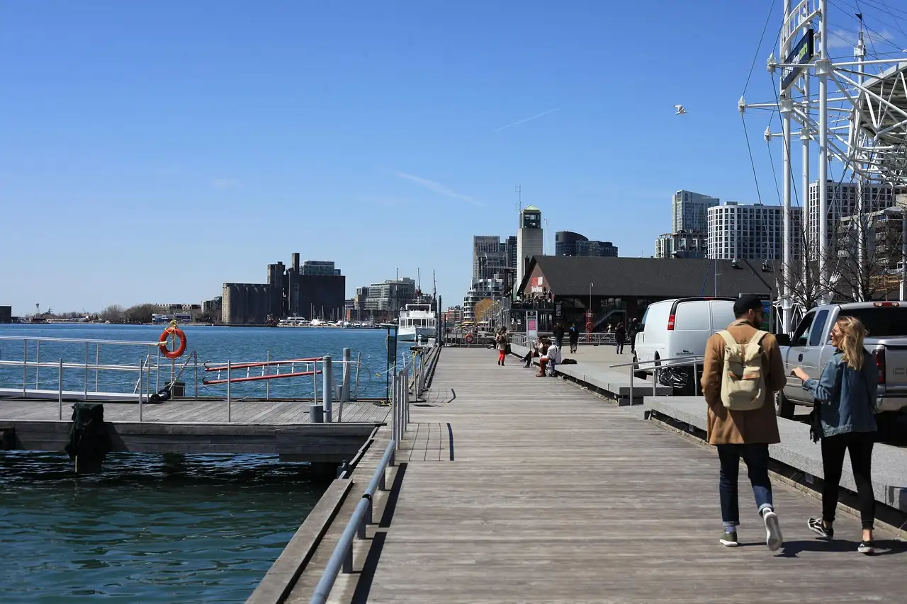 Gente paseando por un paseo de madera junto al agua, en el frente portuario de Toronto