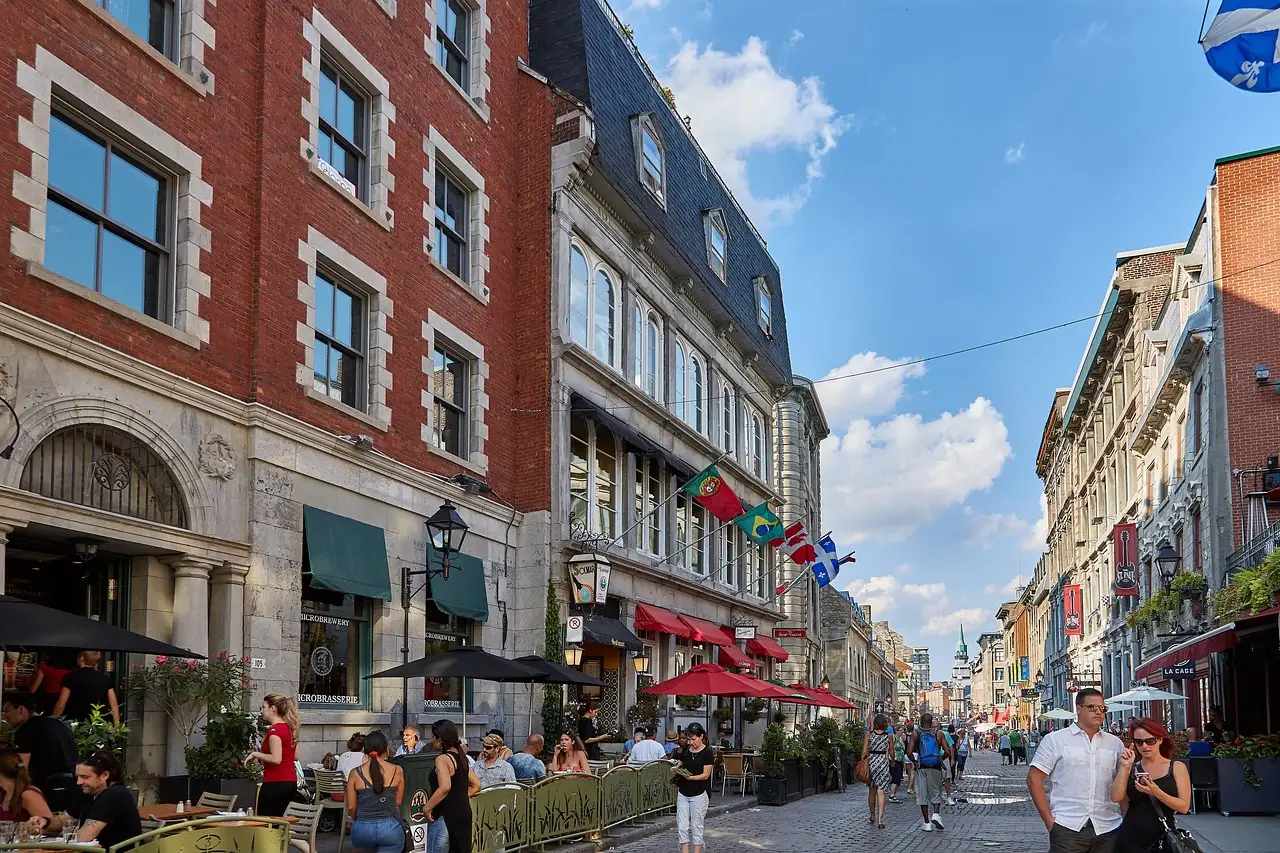 Una calle peatonal del Viejo Montreal con edificios de piedra y ladrillo, terrazas de cafés y gente paseando.