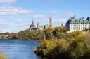 Los edificios de Parliament Hill, en Ottawa, sobre un promontorio junto al río Ottawa, con árboles de otoño en la orilla.