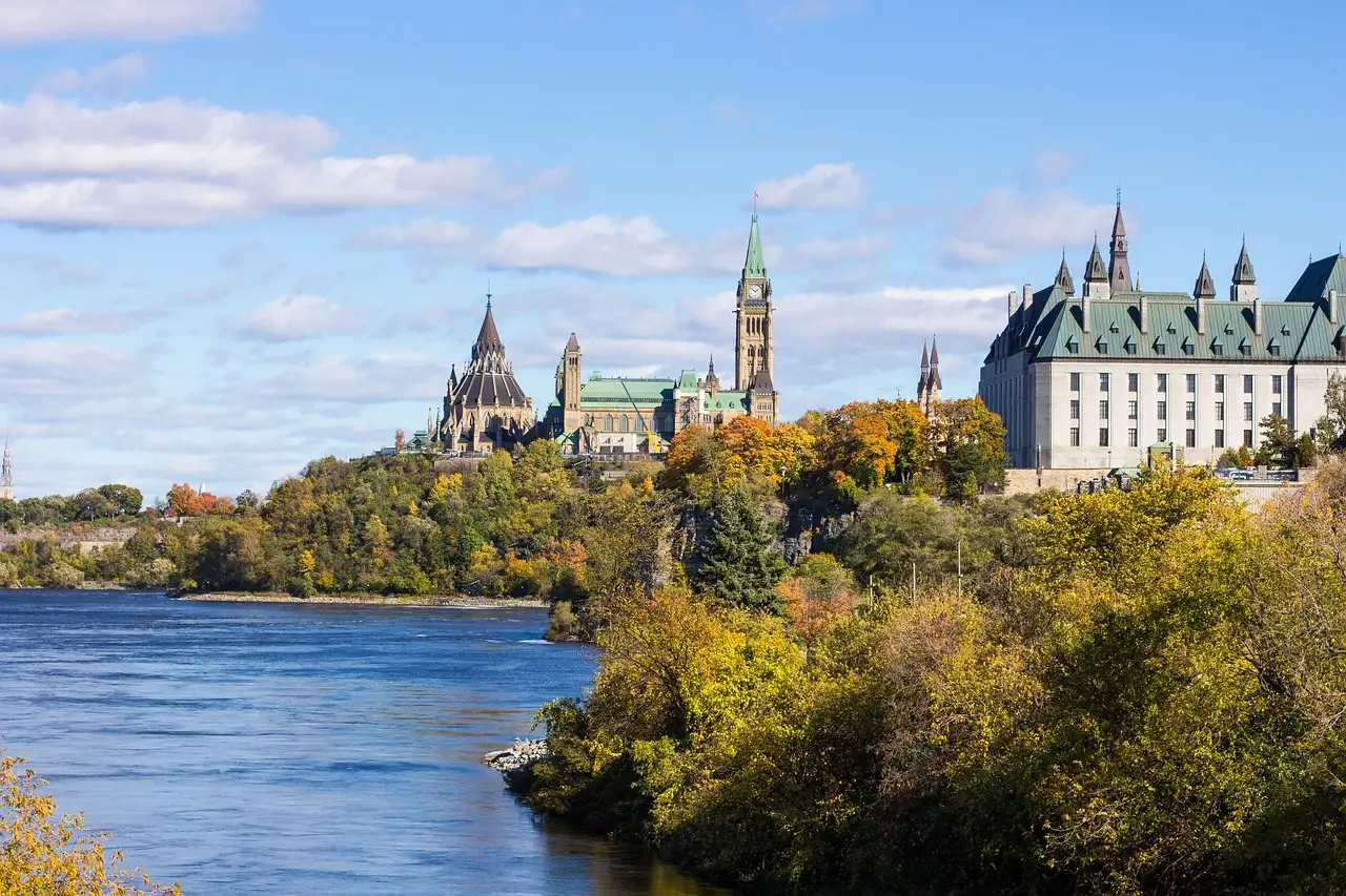 Los edificios del Parlamento de Ottawa sobre una colina junto al río Ottawa, con árboles otoñales en la orilla.