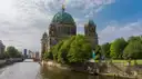 The green-domed Berlin Cathedral seen across the Spree behind leafy trees on a cloudy day