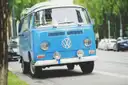 A blue vintage VW bus parked at the roadside under trees