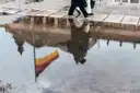 Rain puddle reflecting the Reichstag building and a German flag while two people walk past