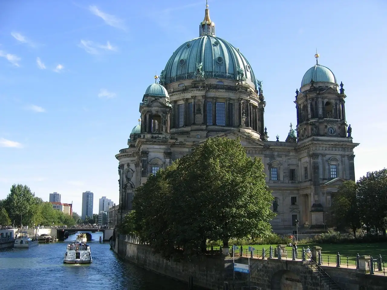 The Berlin Cathedral with its green domes above trees on the bank of the Spree