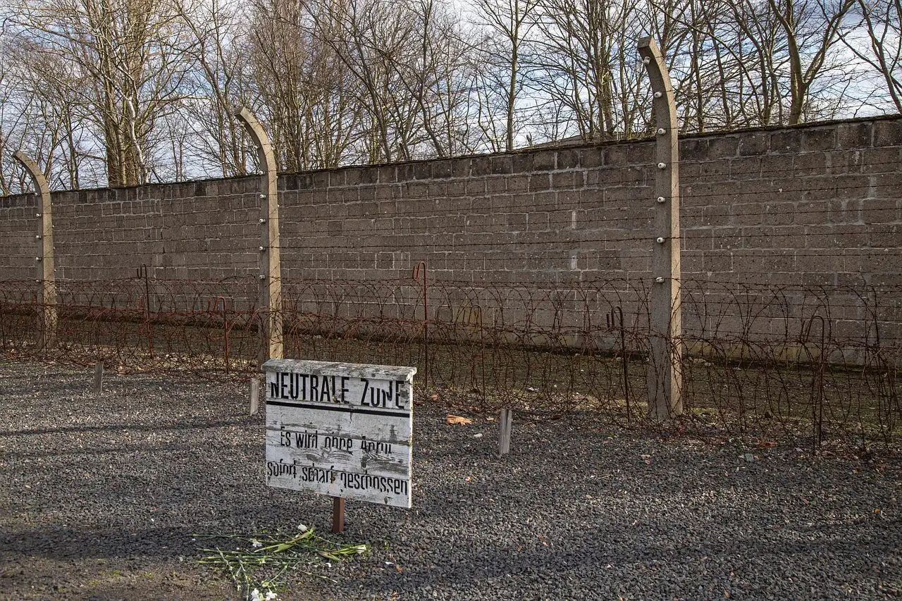 The grey camp wall with posts and wire at the Sachsenhausen Memorial, with a sign in front