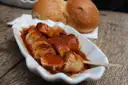 Sliced currywurst in curry ketchup on a white dish, with two bread rolls behind it