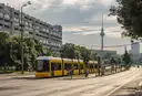 A yellow tram on a wide Berlin street with the TV Tower in the distance