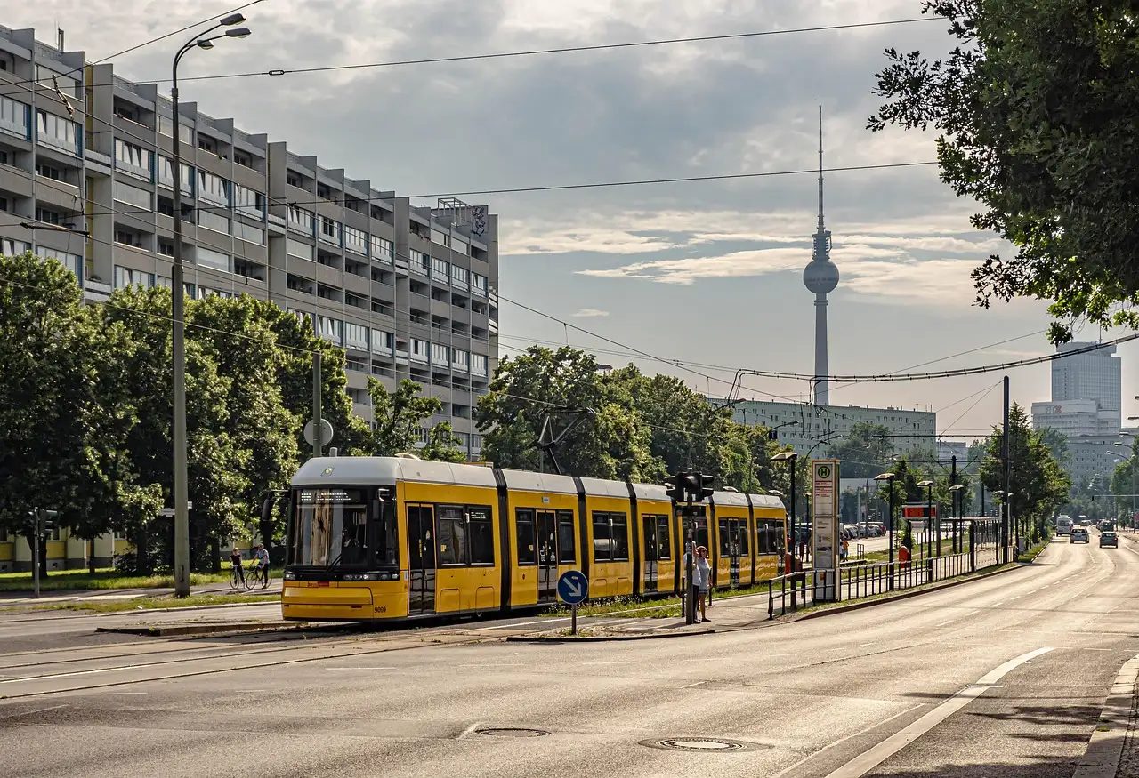 A yellow tram on a wide Berlin street with the TV Tower in the distance