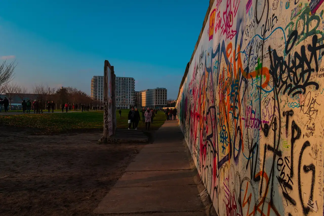 A graffiti-covered stretch of the Berlin Wall beside a path at dusk