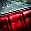 Three red seats on the upper deck of an open-top sightseeing bus, with people crossing the street below