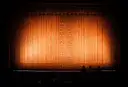 An empty theater stage behind a glowing orange curtain