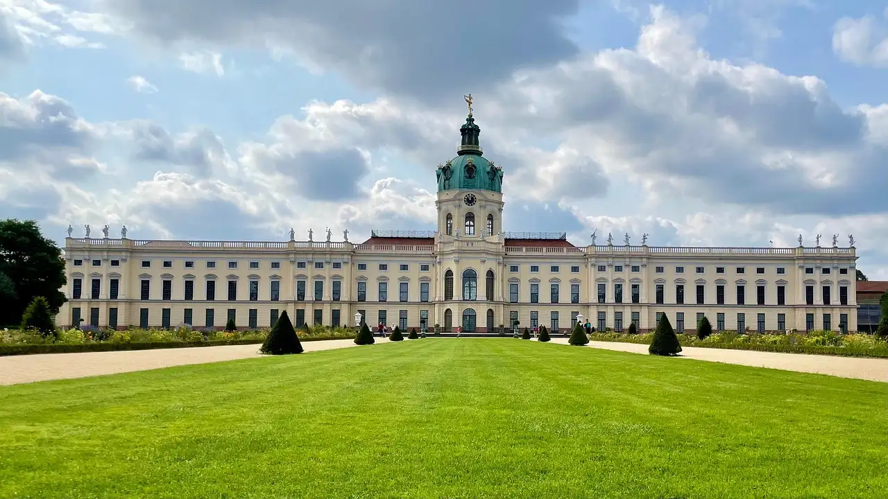 Charlottenburg Palace with its green-domed tower behind a wide lawn under a cloudy sky