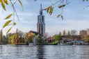 A tall church tower and houses on the bank of the Havel in Potsdam, framed by autumn leaves