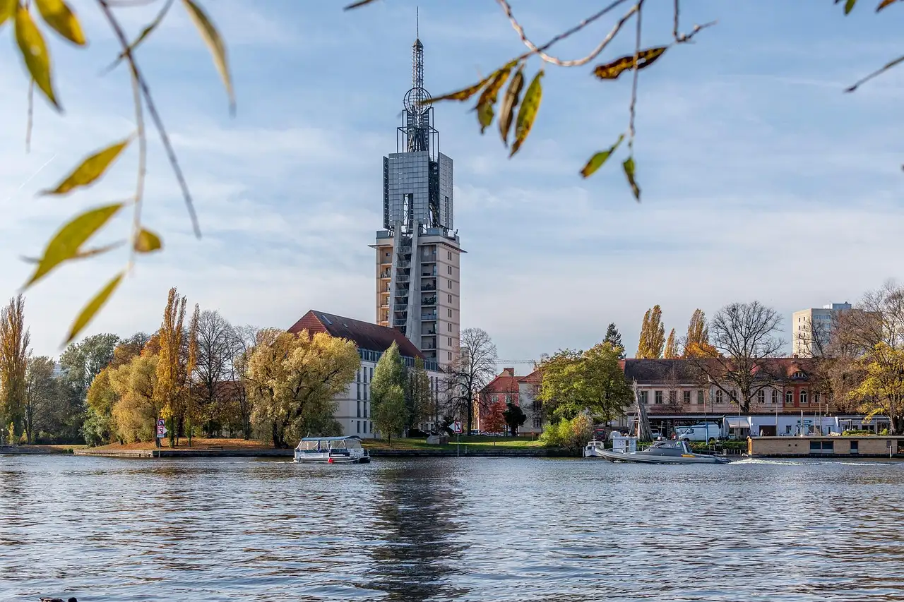 A tall church tower and houses on the bank of the Havel in Potsdam, framed by autumn leaves