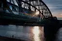 A train crossing a steel arch railway bridge over the Vltava in Prague at sunset