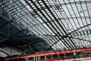 A red regional train under the vast glass and steel roof of Berlin Hauptbahnhof