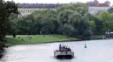 A small boat on the Landwehr Canal, with people on the grass bank