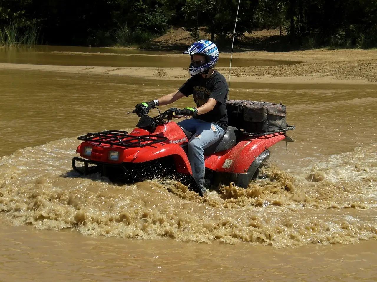 A rider in a helmet driving a red ATV through brown muddy water