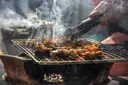 Meat cooking on a smoky open grill, turned with tongs