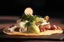 A meat taco topped with avocado and herbs on a dark plate