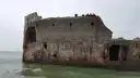 The broken hull of an old concrete ship sitting in calm green water