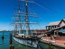 A three-masted tall ship tied up at a wooden pier in the Galveston harbor