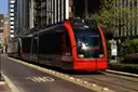 A red METRORail light rail train on a downtown Houston street between tall buildings