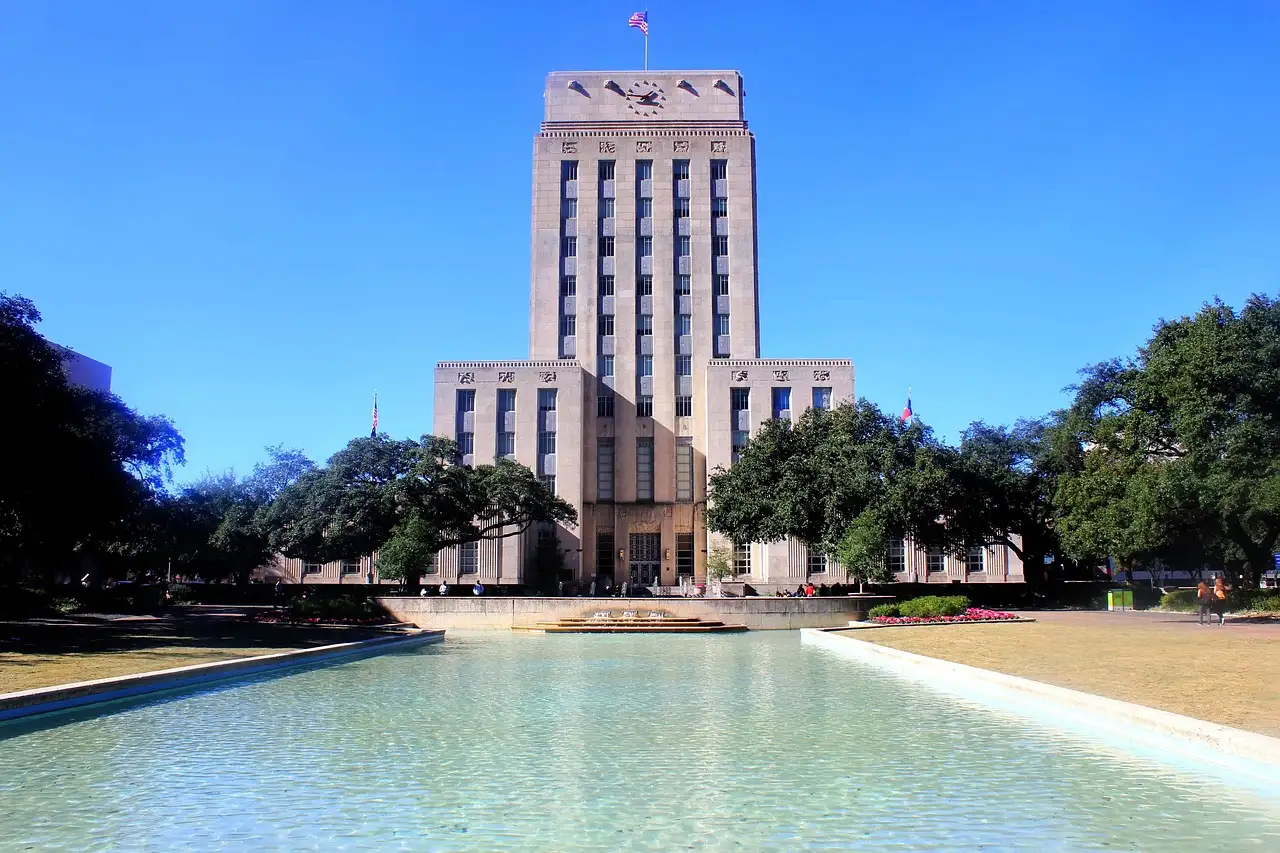 Houston City Hall, a pale stone tower, behind its long reflecting pool on a sunny day