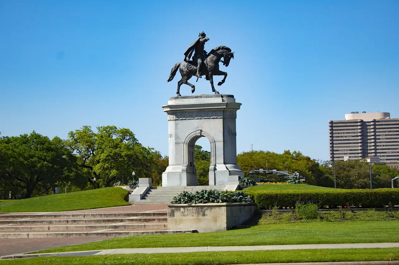 The Sam Houston statue on horseback atop a stone arch in Hermann Park, under a blue sky