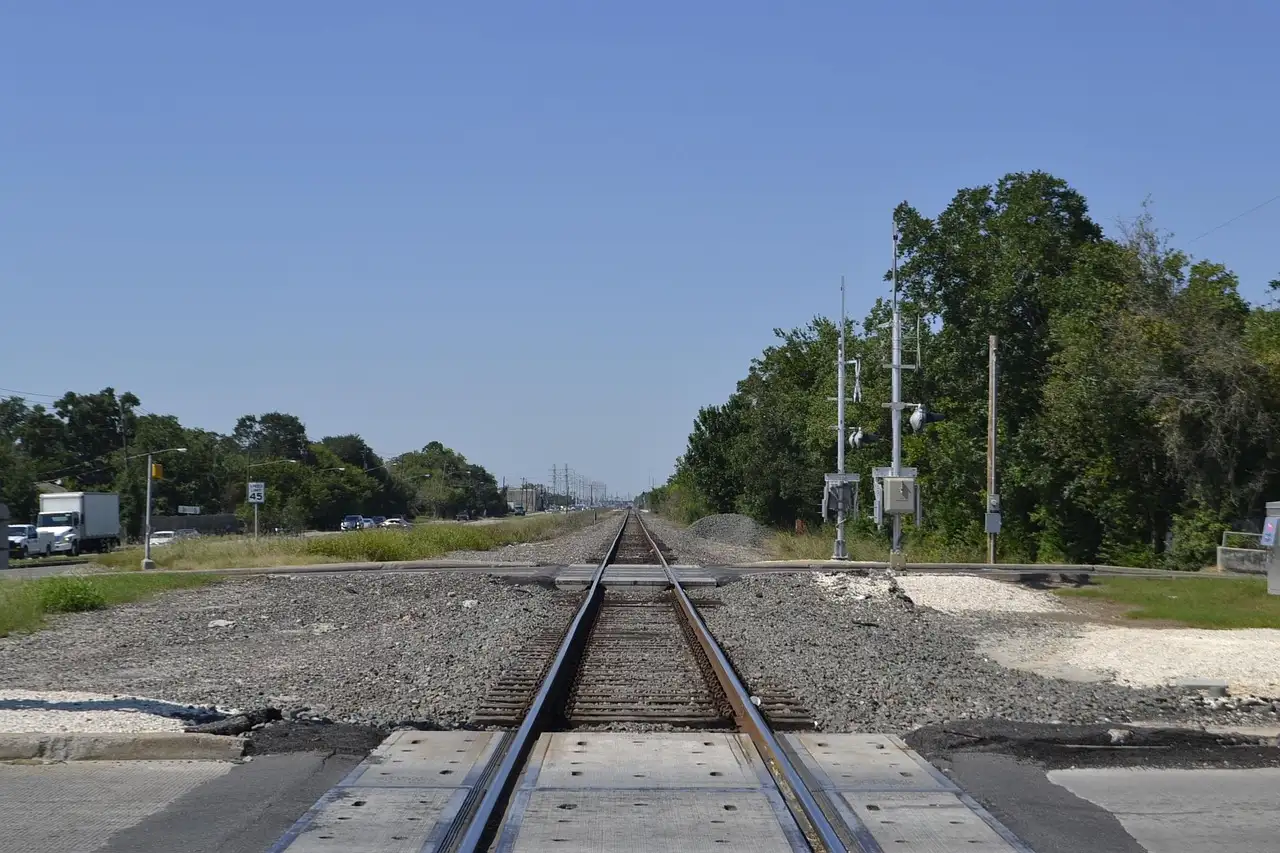 Empty railway tracks crossing a road in Houston under a wide blue sky, with no train in the picture